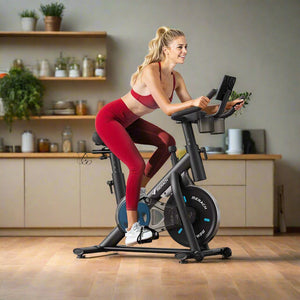 A woman is using a black Magnetic Resistance Exercise Bike with adjustable seat and resistance settings. The bike is placed in a home gym setup with Christmas decorations around it.