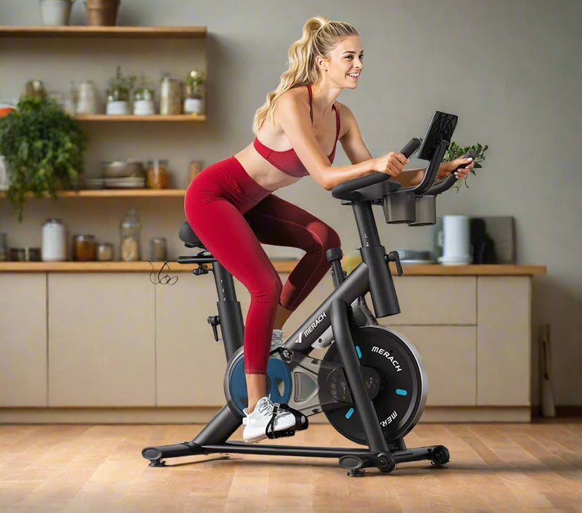 A woman is using a black Magnetic Resistance Exercise Bike with adjustable seat and resistance settings. The bike is placed in a home gym setup with Christmas decorations around it.