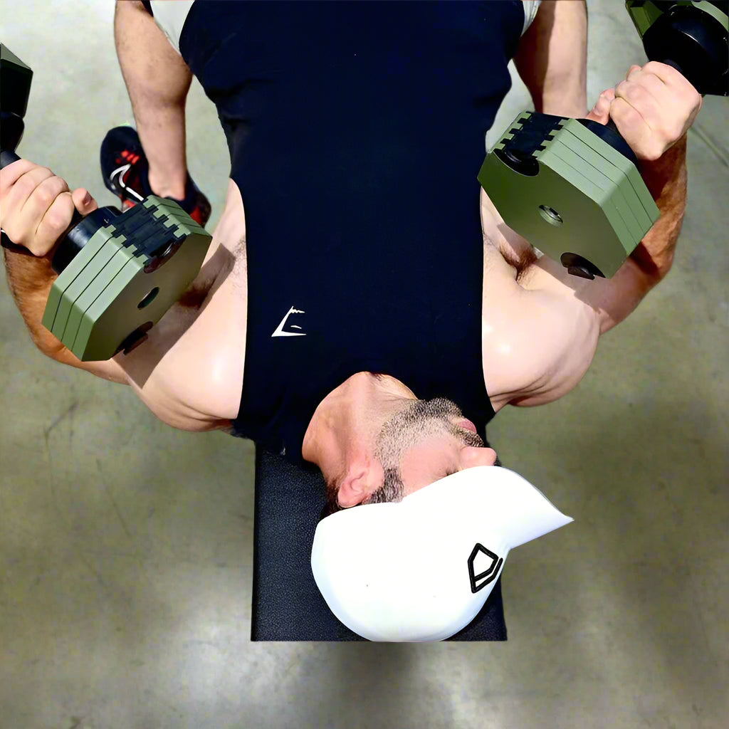 Person exercising with dumbbells on a road, wearing a black shirt with a logo and a white cap.
