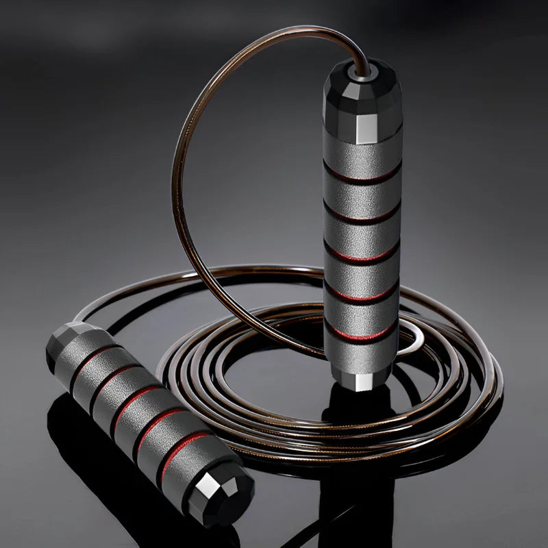 An adjustable jump rope with steel wire and black and red handles lying on a reflective surface.