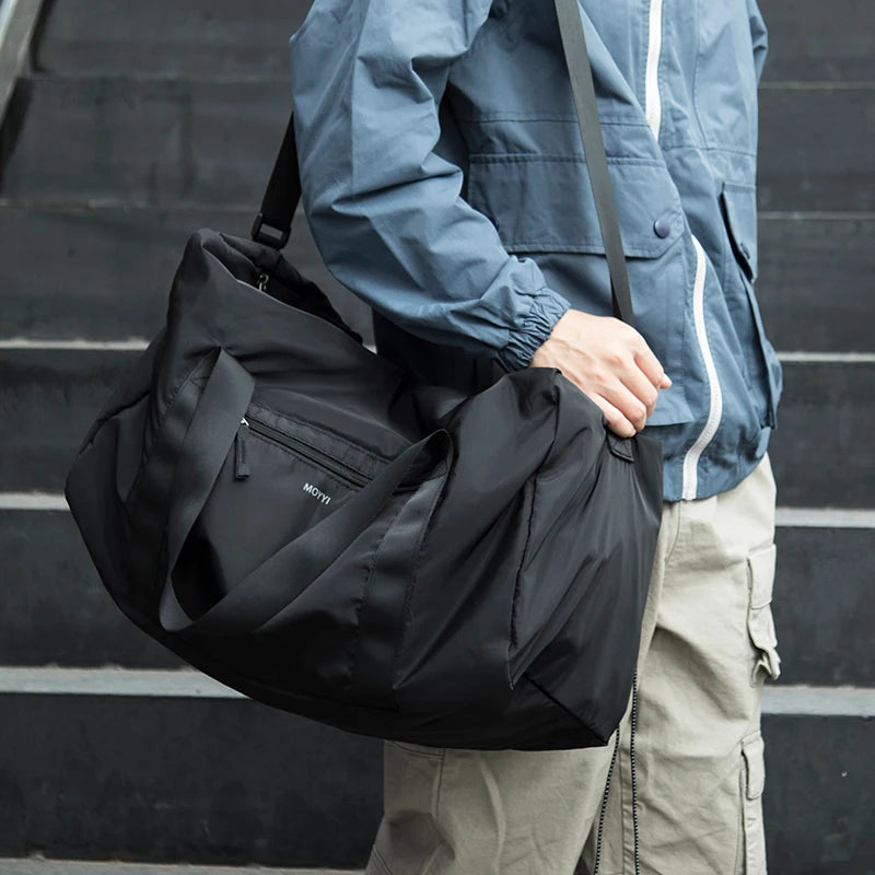 A person carrying a large black duffle bag with zipper closure. The bag appears to be made of a nylon material and has a shoulder strap for carrying.